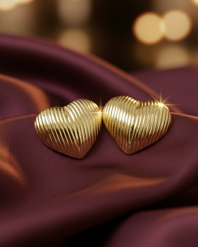 Gold heart-shaped earrings on a dark fabric background with blurred lights