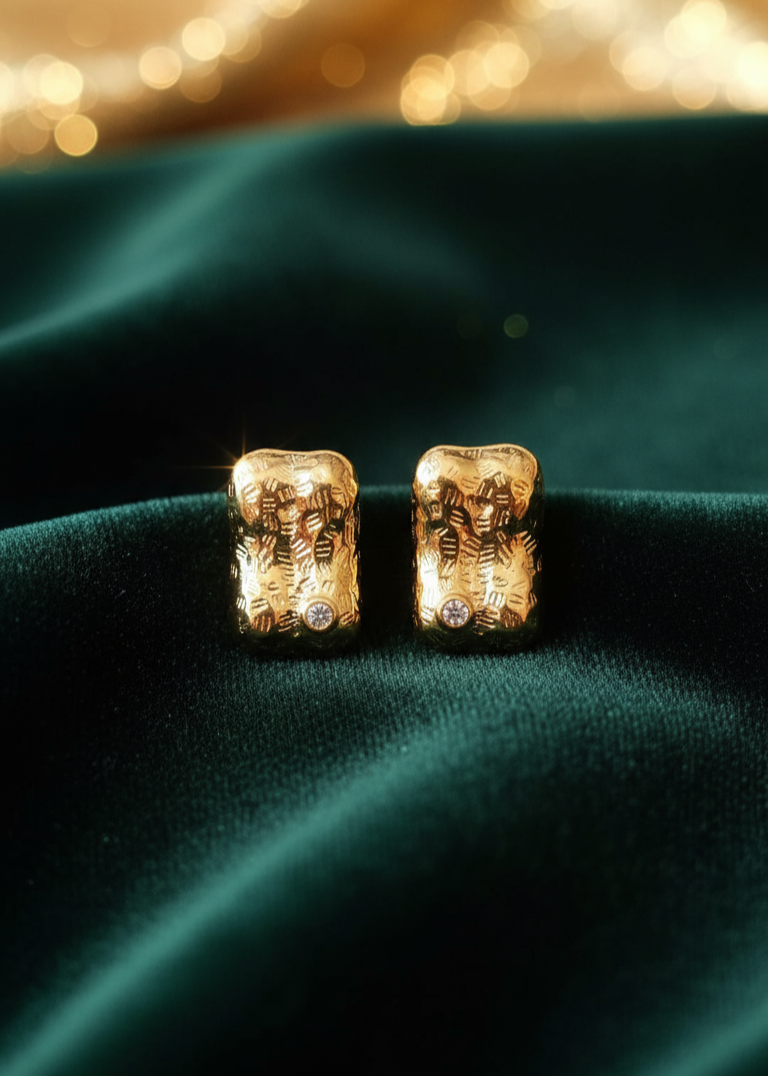 Gold earrings with intricate designs on a green fabric background