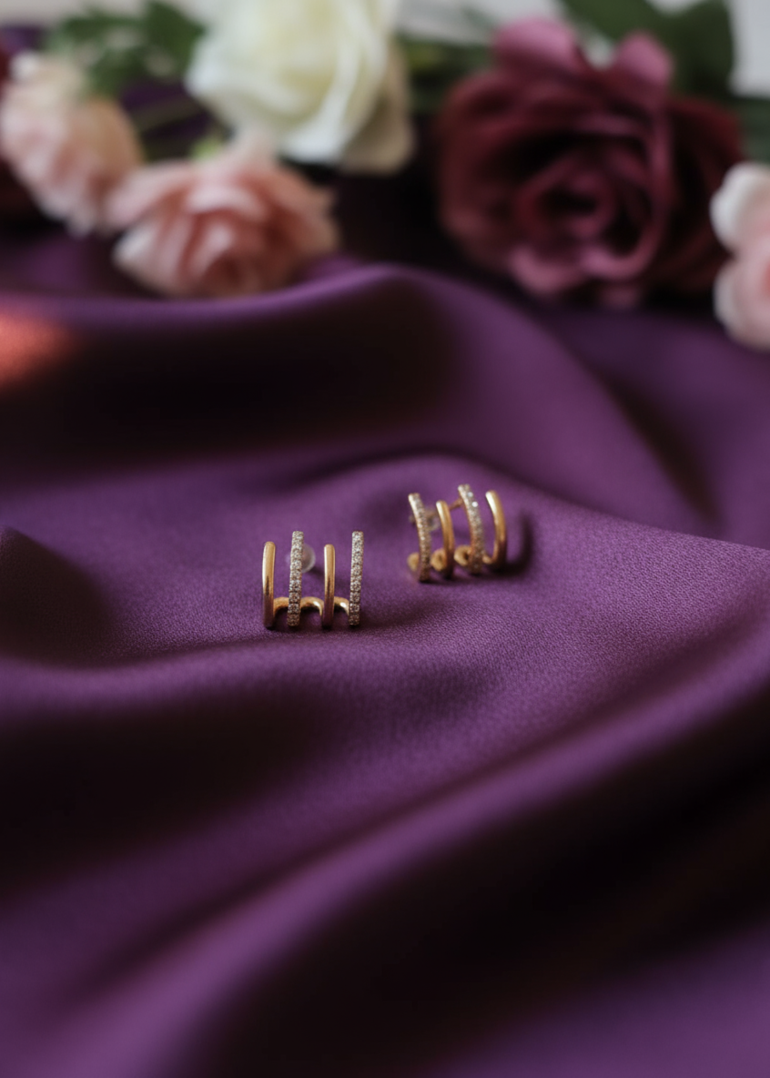 Gold earrings on a purple fabric with blurred flowers in the background