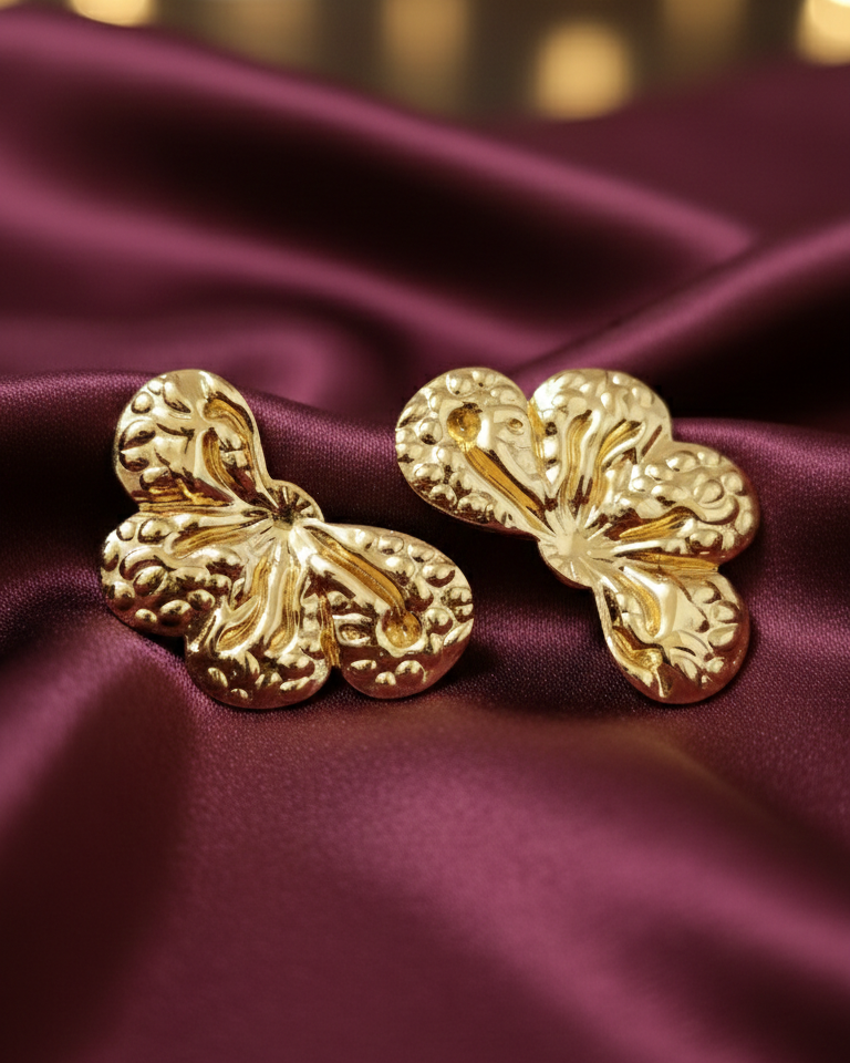 Gold flower-shaped earrings on a burgundy fabric with blurred lights in the background
