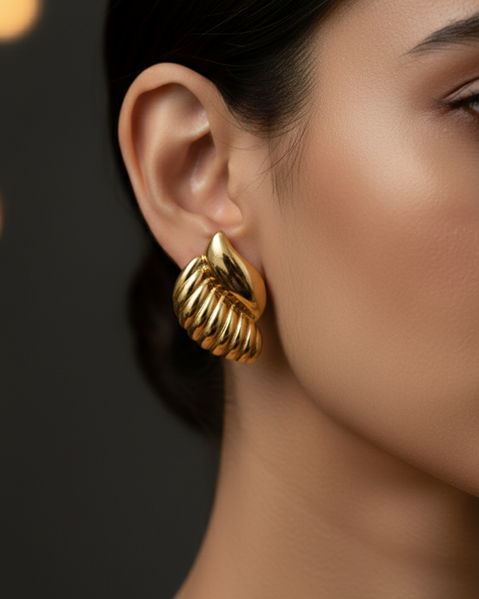 Gold earrings worn by a model against a dark background