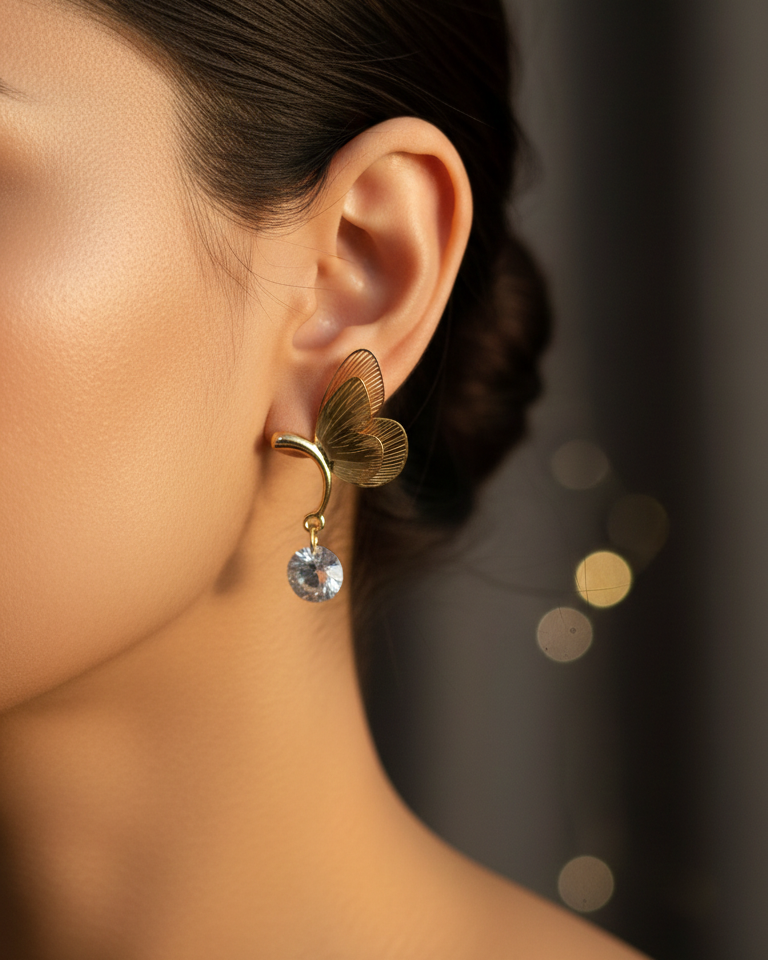 Close-up of a woman wearing a gold earring with a clear gemstone against a blurred background.