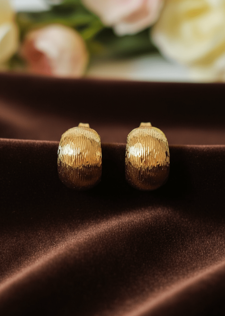 Gold earrings on a brown surface with blurred flowers in the background