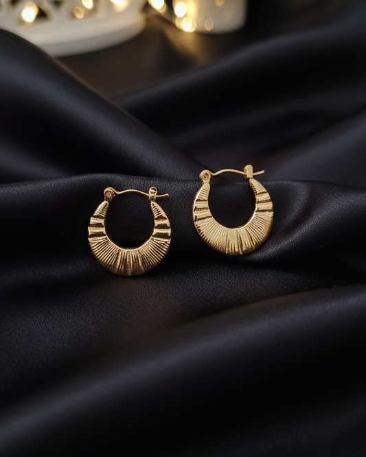 Gold hoop earrings on a black fabric background with blurred lights in the background