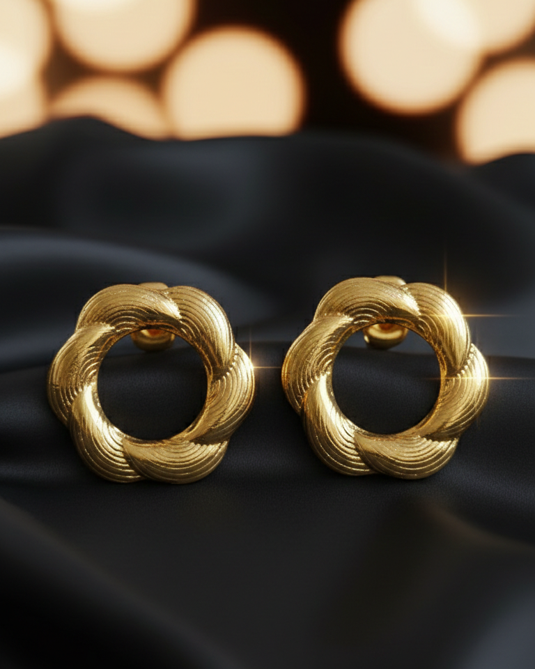 Pair of gold earrings on a black fabric background with blurred lights