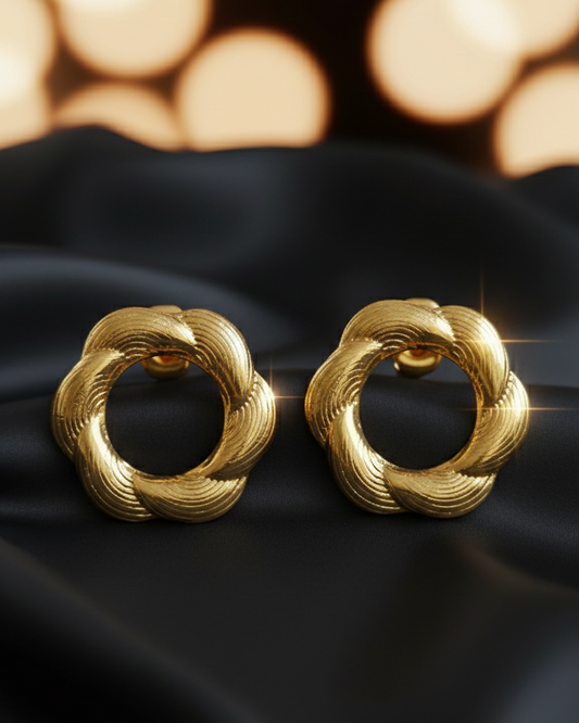 Pair of gold earrings on a black fabric background with blurred lights