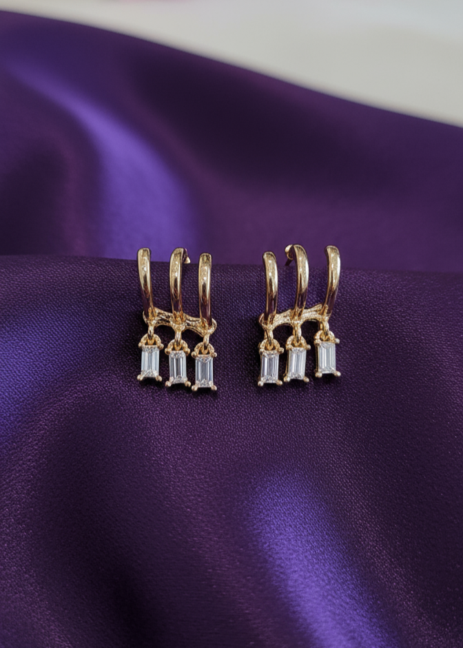 Gold earrings with clear stones on a purple fabric background