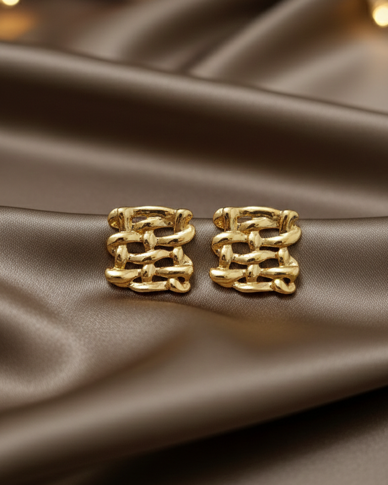 Gold earrings on a brown satin surface with blurred lights in the background