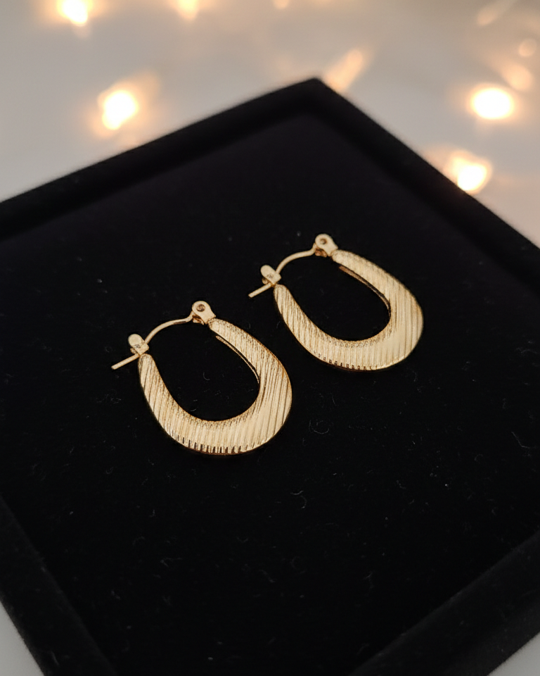 Gold hoop earrings on a black display box with string lights in the background