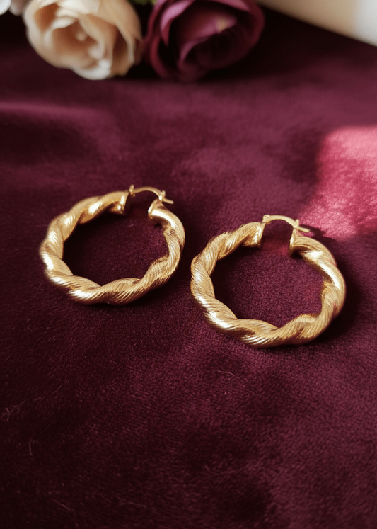 Gold hoop earrings on a burgundy fabric background with flowers.