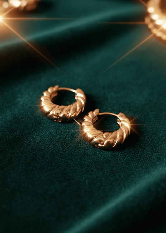 Gold hoop earrings on a dark green fabric background