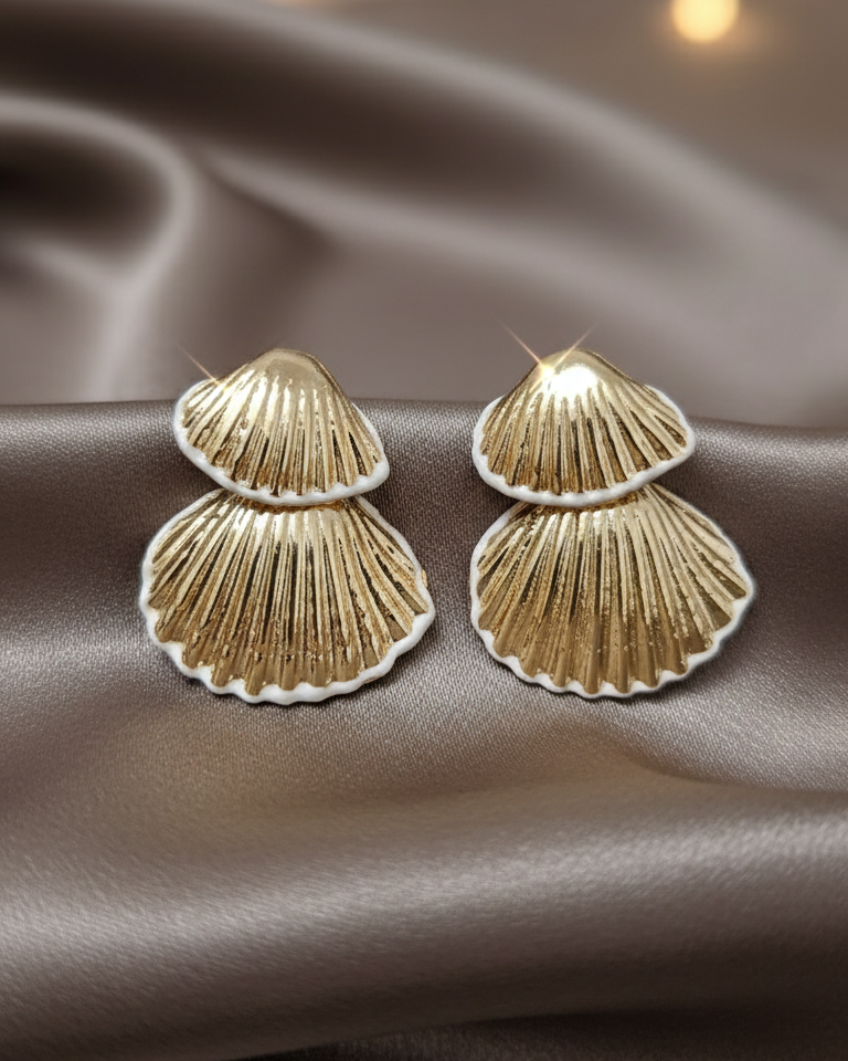 Gold shell-shaped earrings on a brown fabric background with blurred lights.