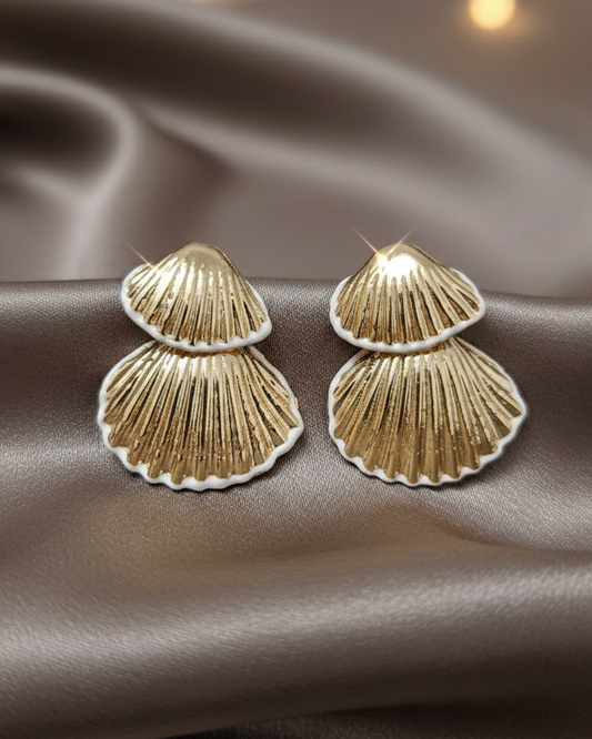 Gold shell-shaped earrings on a brown fabric background with blurred lights.