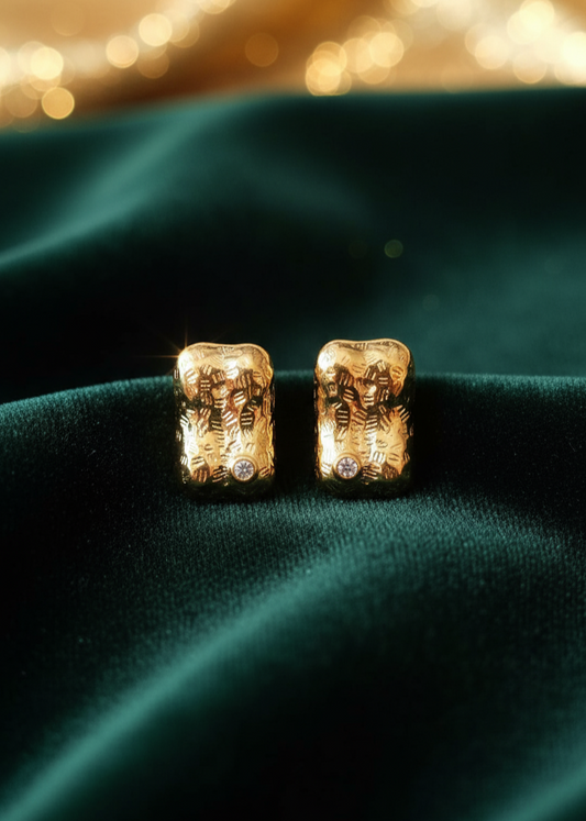 Gold earrings with intricate designs on a green fabric background