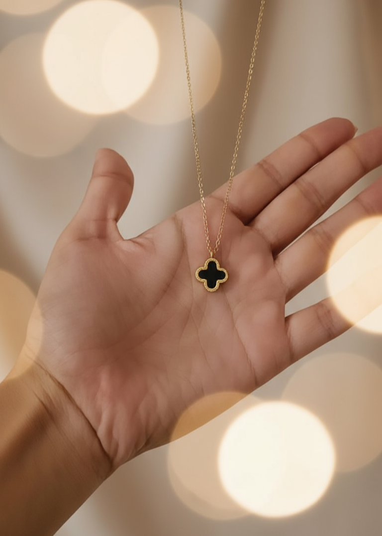 Hand holding a gold necklace with a clover pendant against a blurred light background