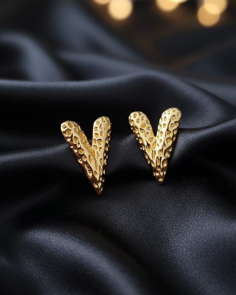 Gold 'V' shaped earrings on a dark fabric background