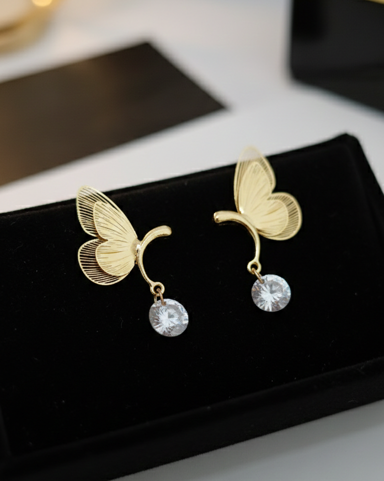 Gold butterfly earrings with pearl drops on a black stand.