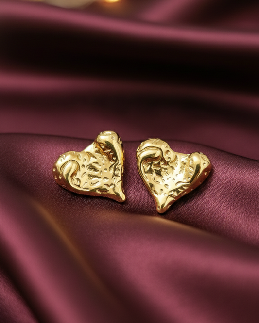 Gold heart-shaped earrings on a burgundy fabric background