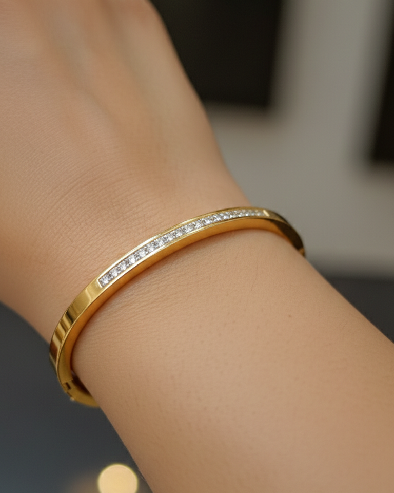 Gold bracelet with diamond accents on a wrist against a blurred background
